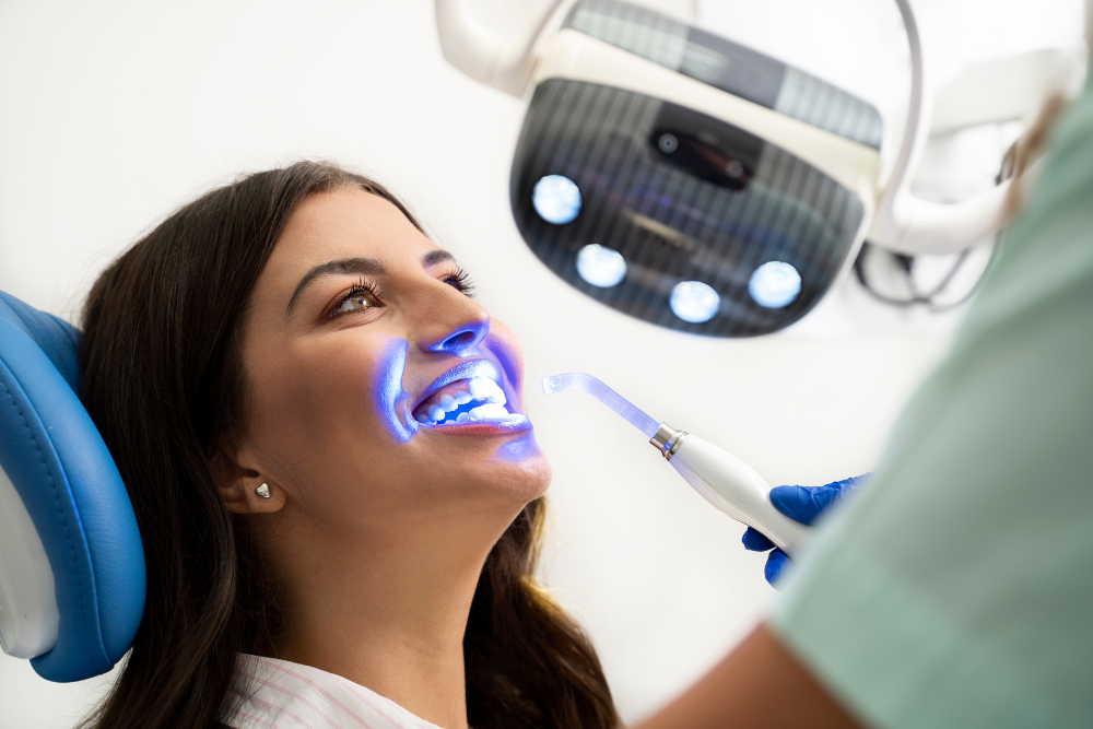 A woman is sitting in a dental chair getting her teeth whitened by a dentist.