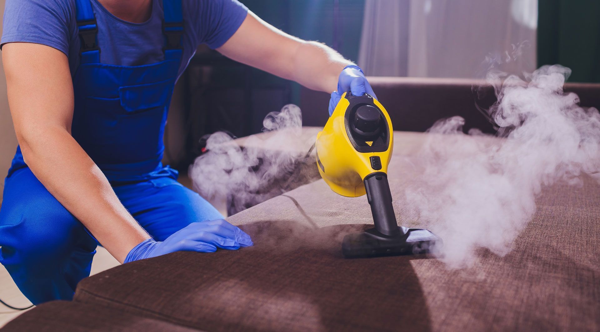 A man is cleaning a couch with a steam cleaner.
