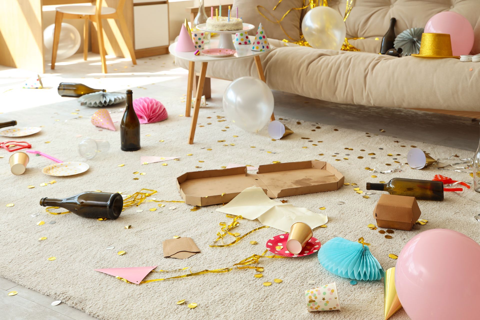 A messy living room after a party with balloons , plates , bottles and confetti on the floor.