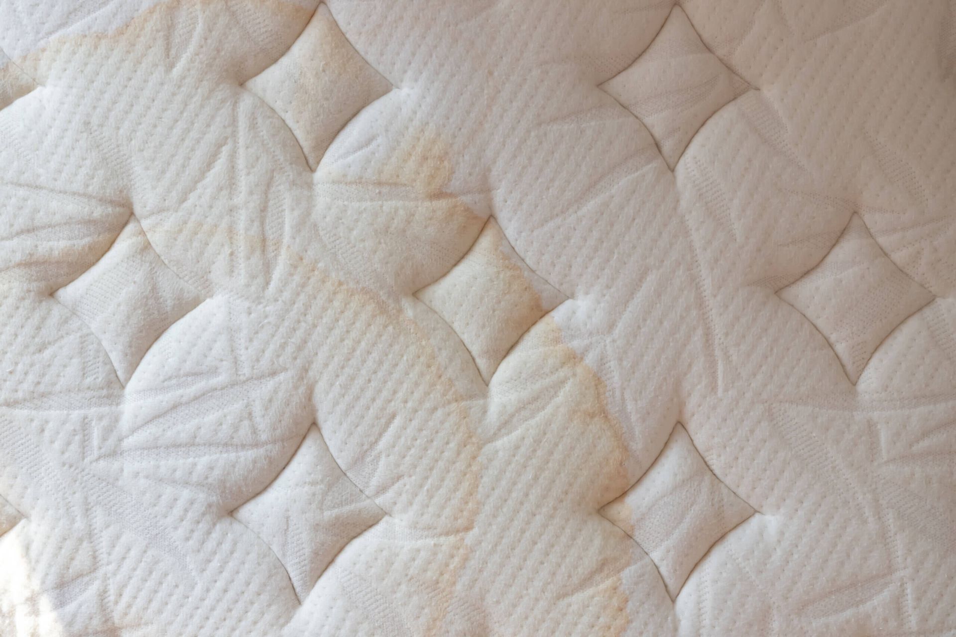 A close up of a white mattress with stains on it.