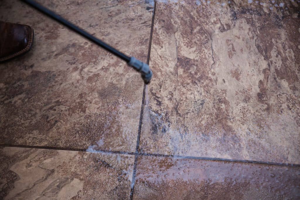 A person is using a high pressure washer to clean a tile floor.