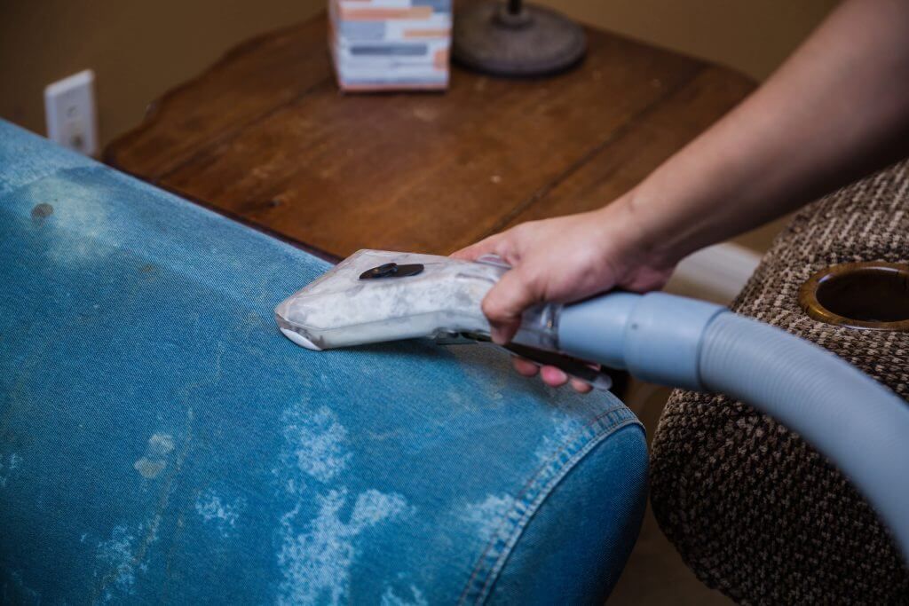 A person is cleaning a blue couch with a vacuum cleaner.