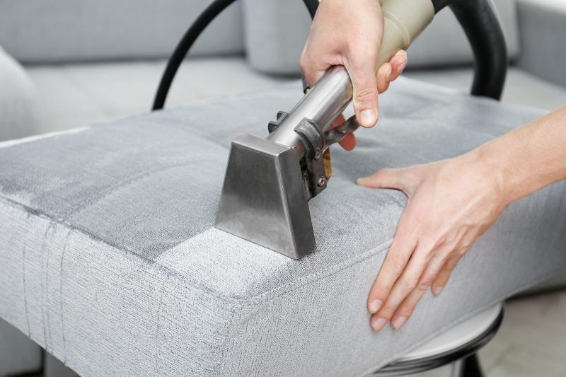 A person is cleaning a couch with a vacuum cleaner.