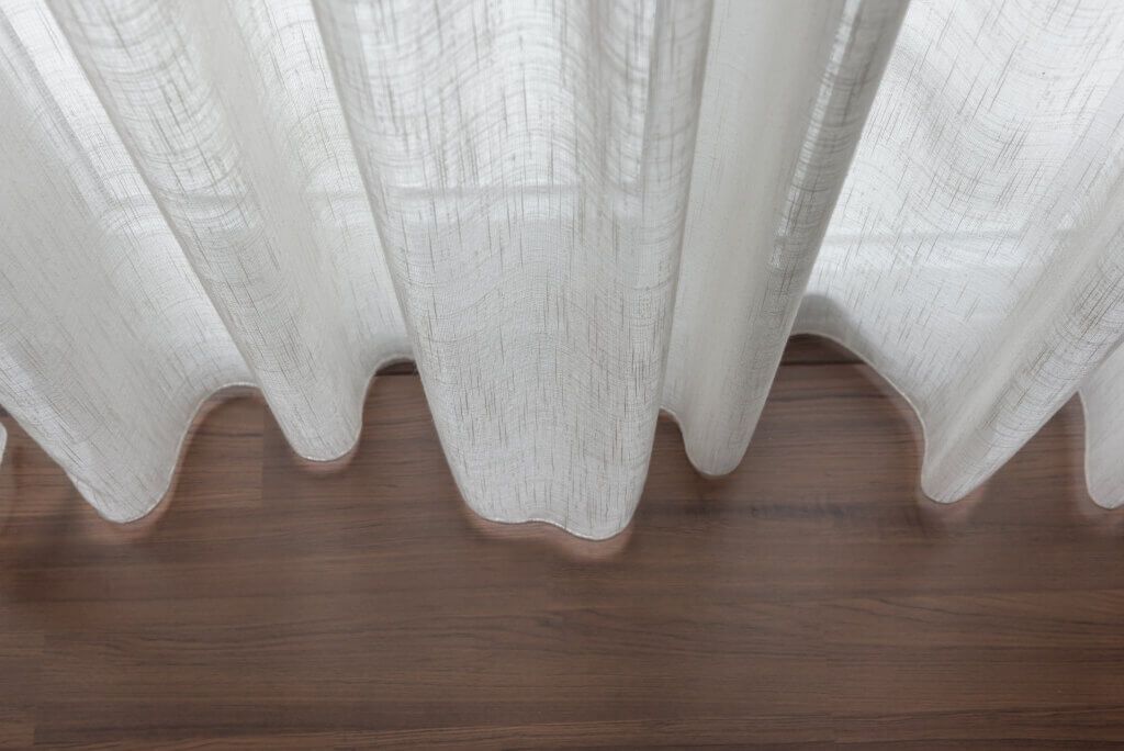 A white curtain is hanging on a wooden window sill.