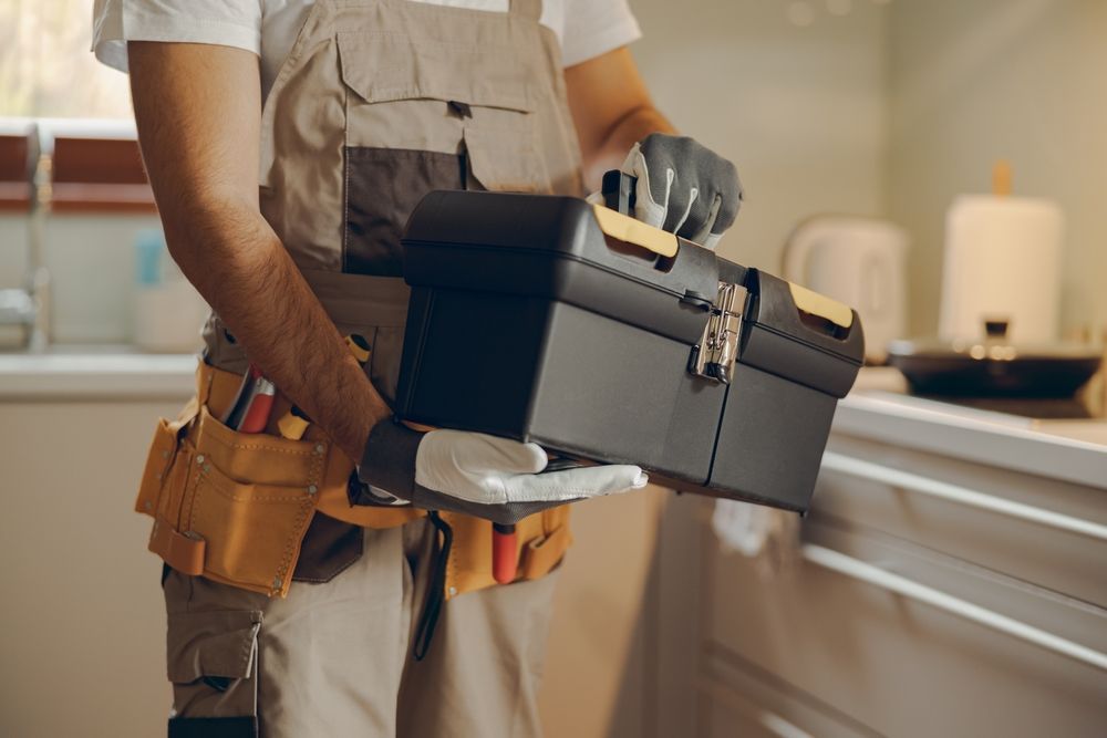 A man is holding a toolbox in his hands in a kitchen.