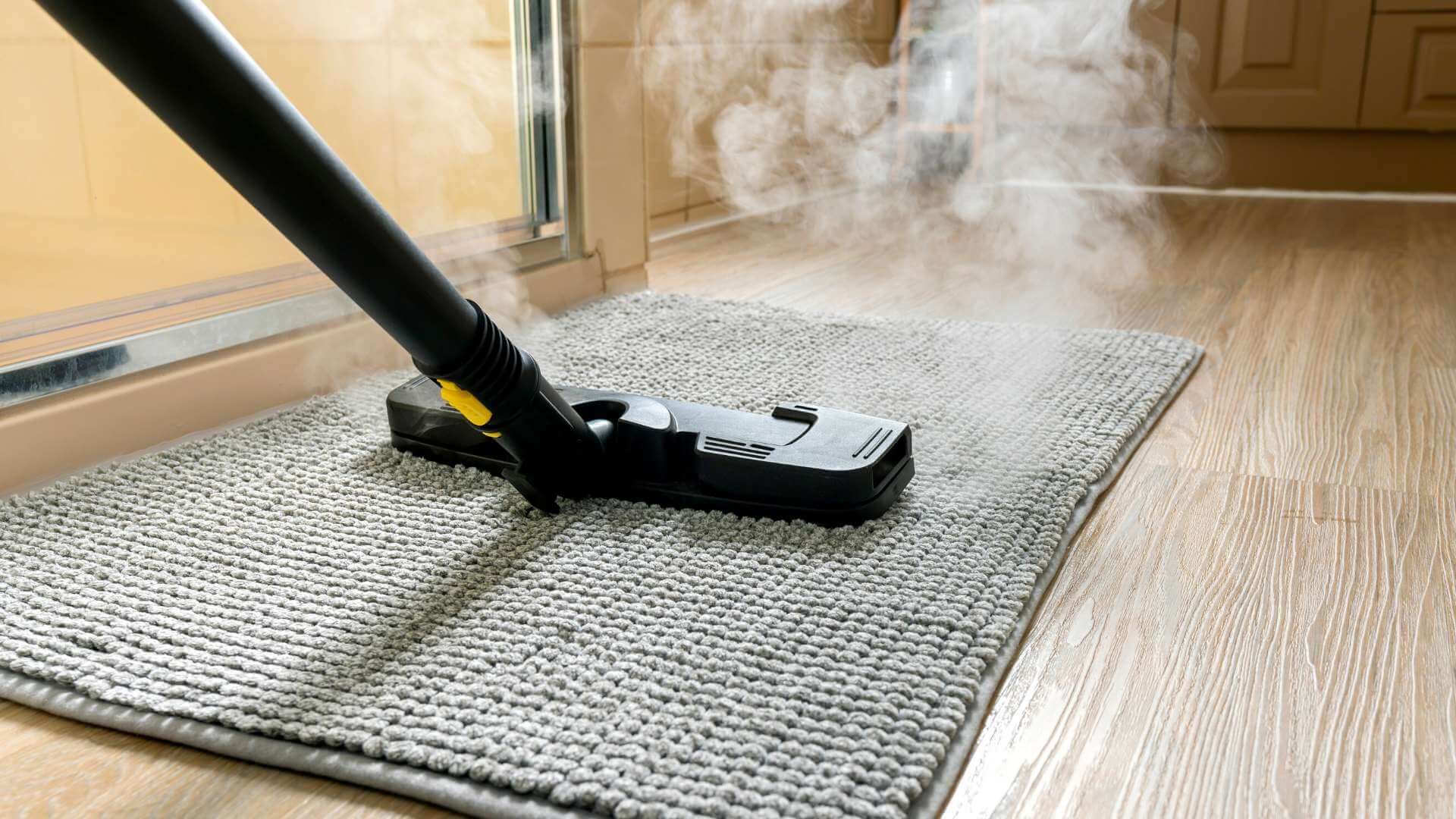 A vacuum cleaner is cleaning a rug on a wooden floor.