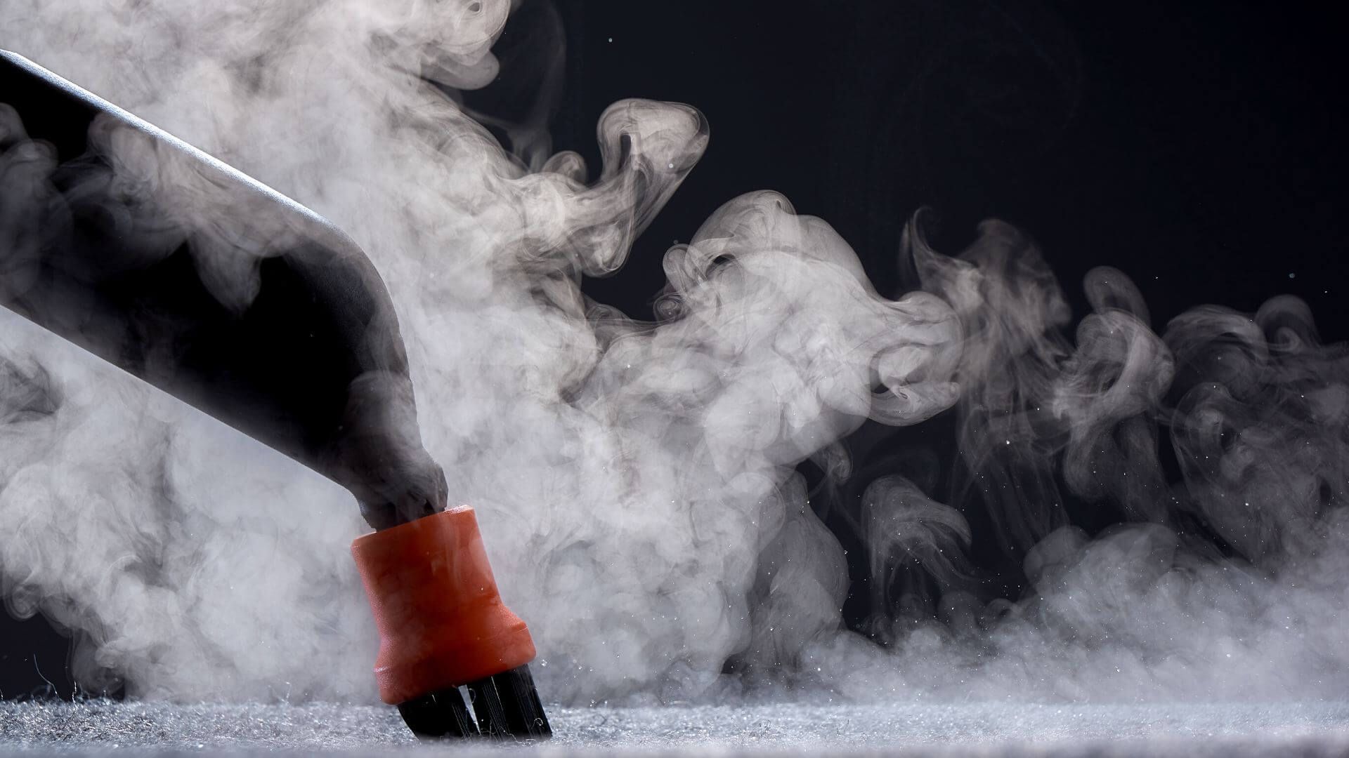 A person is using a steam cleaner to clean a carpet with smoke coming out of it.