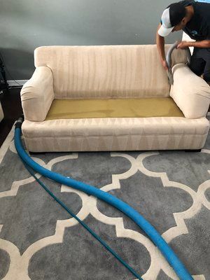 A man is cleaning a couch with a vacuum cleaner in a living room.
