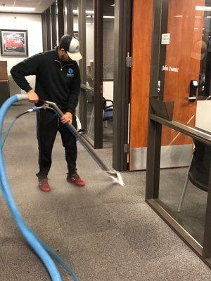A man is cleaning a carpet with a vacuum cleaner in an office.