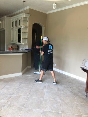 A man is cleaning the floor of a kitchen with a mop.