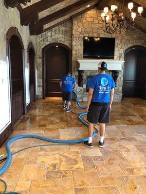 Two men are cleaning a tile floor in a living room.