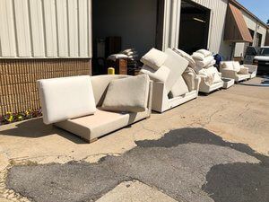 A row of white couches and chairs are sitting outside of a building.