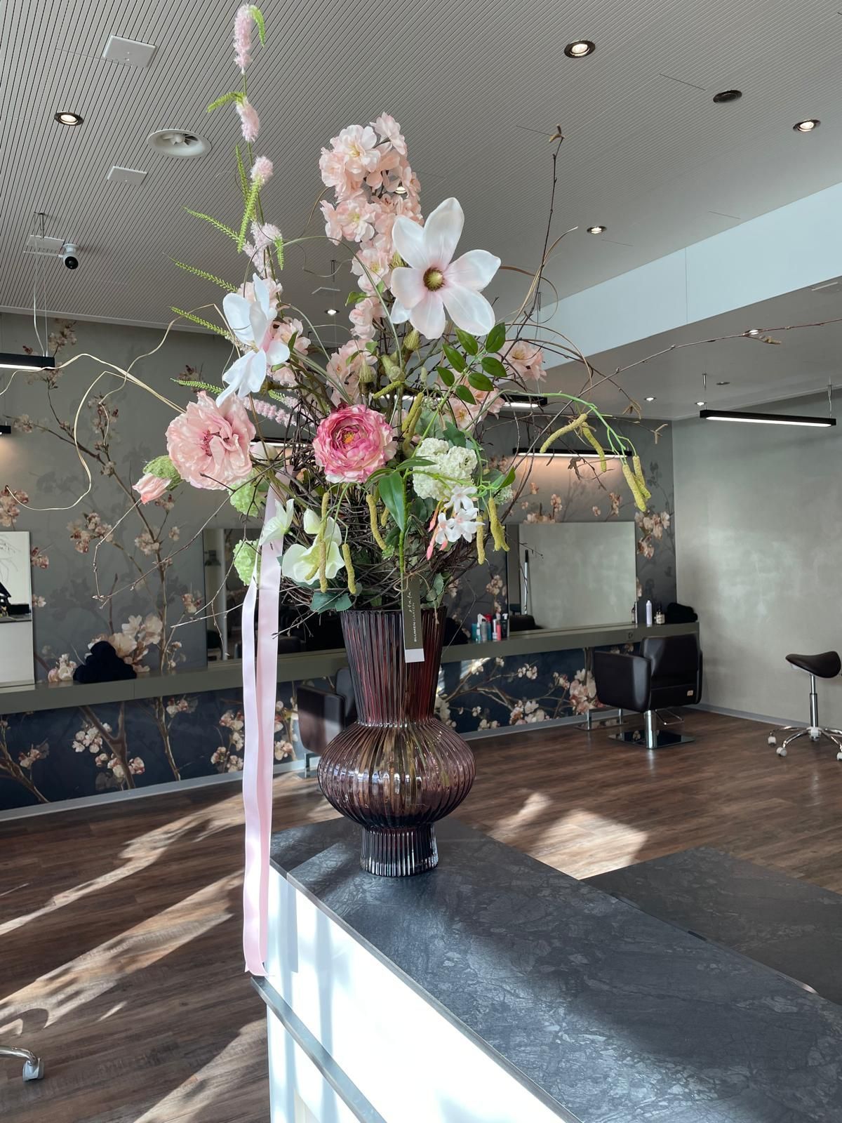 Auf einem Tresen in einem Salon steht eine mit Blumen gefüllte Vase.