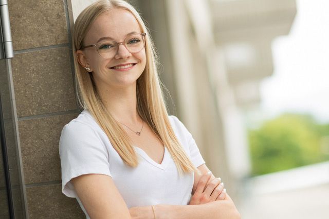 Eine junge Frau in einem weißen T-Shirt lächelt und berührt ihr Haar.