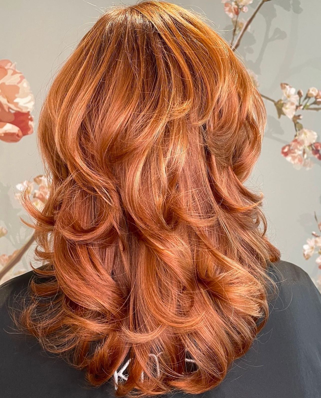 Eine Frau mit langen roten Haaren steht vor Blumen.