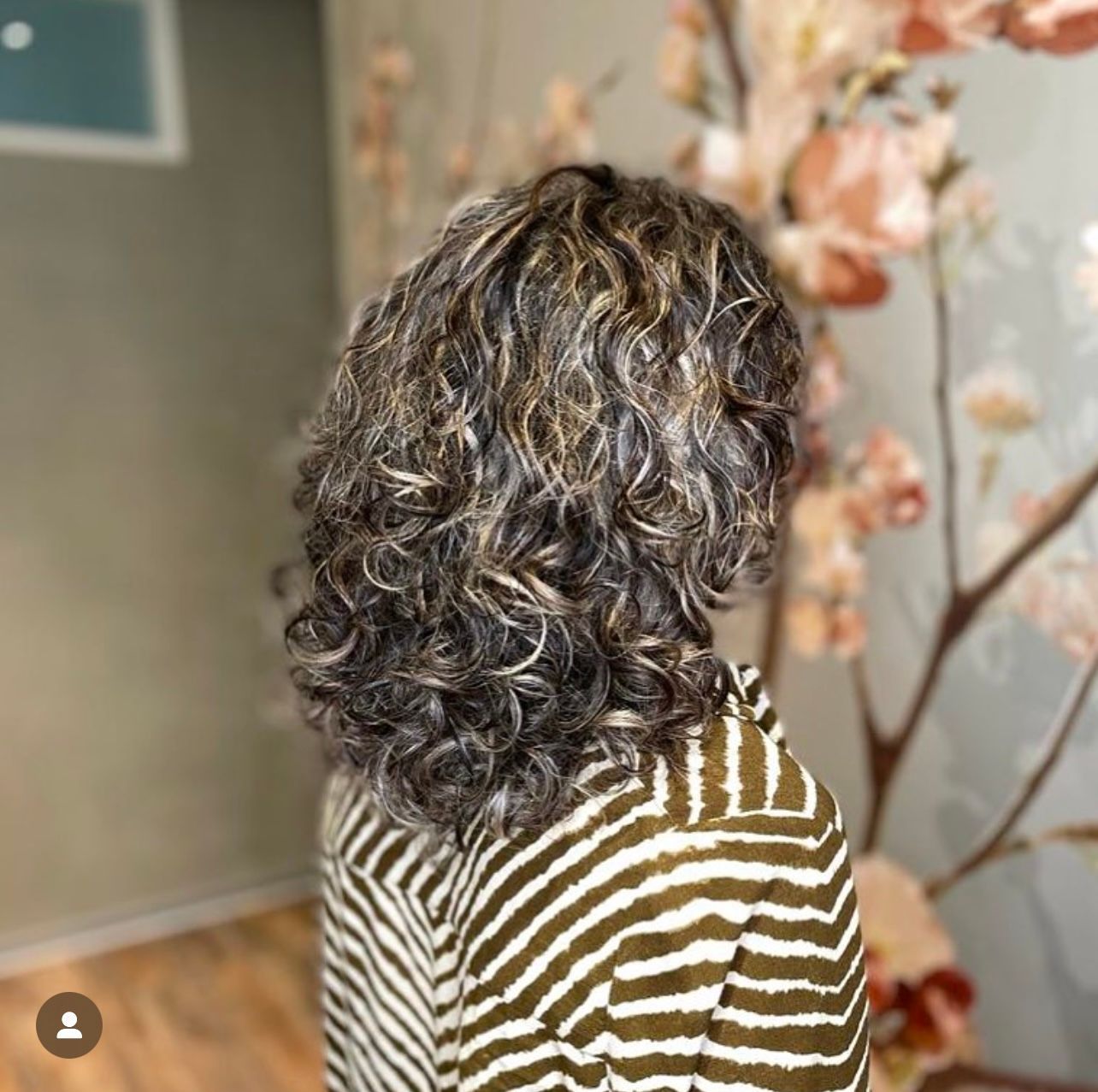 Eine Frau mit lockigem Haar trägt ein gestreiftes Hemd.