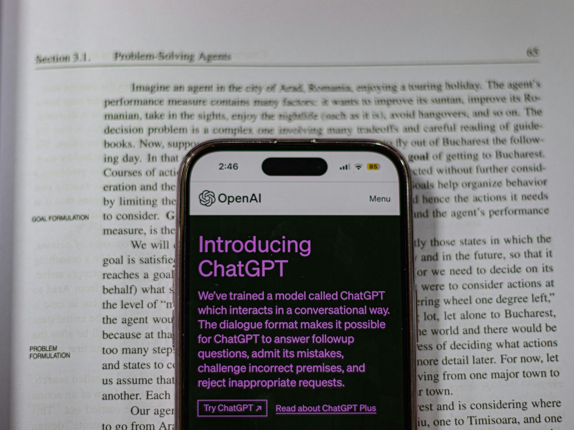 A smartphone displaying the ChatGPT introduction screen rests on an open book.