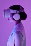Woman in VR headset and headphones, lit by purple light.