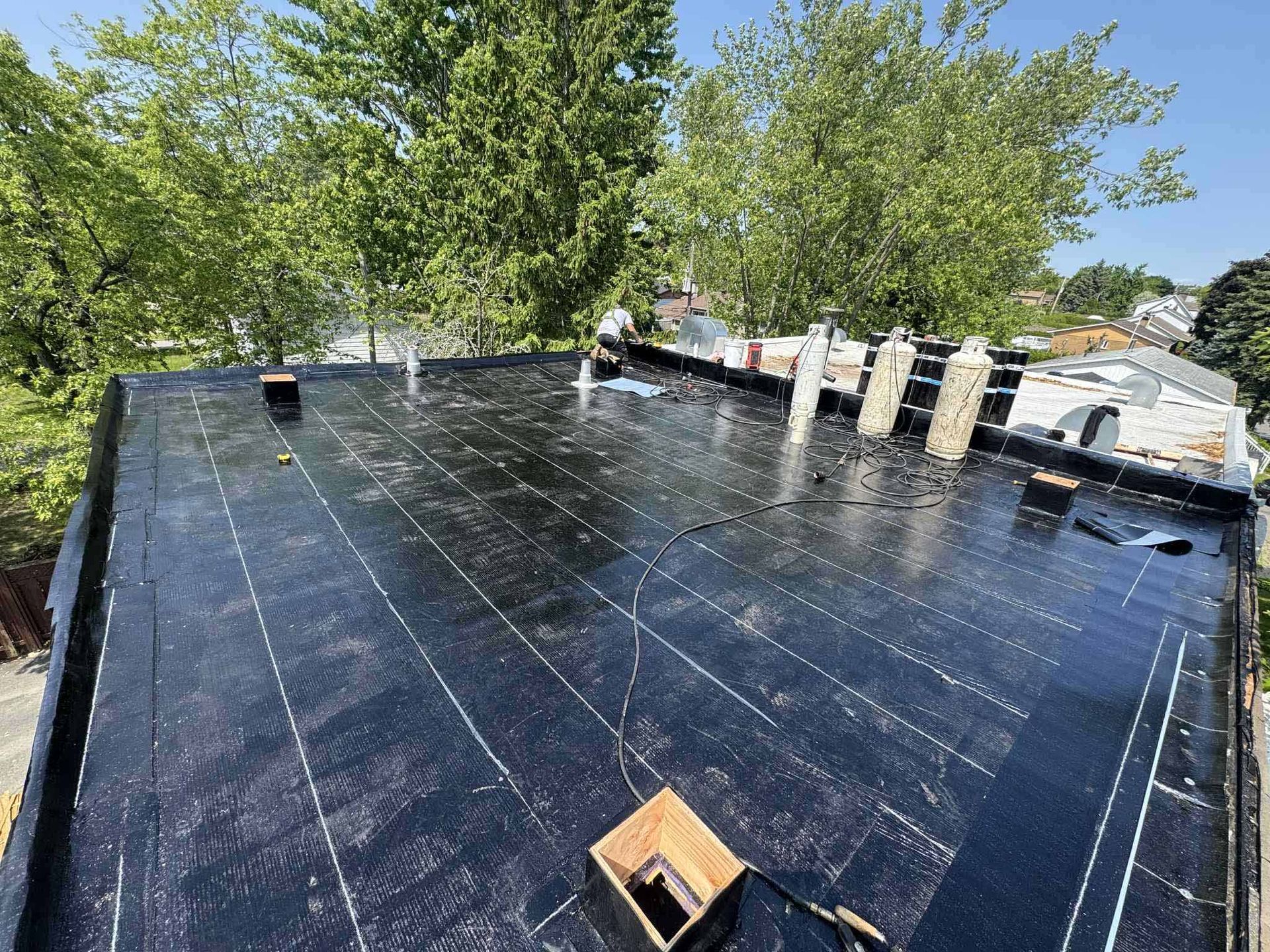Toit plat argenté d'un bâtiment commercial sous un ciel bleu, avec des finitions blanches et un aperçu des bâtiments environnants.