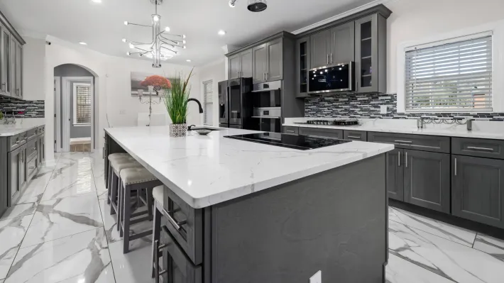 A kitchen with gray cabinets and white counter tops and a large island in the middle.