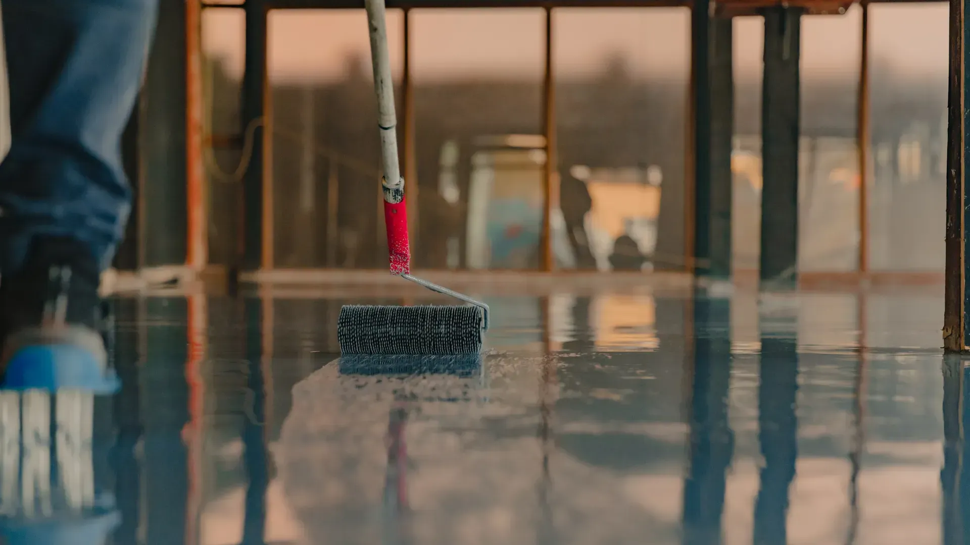 A person is painting a concrete floor with a roller.