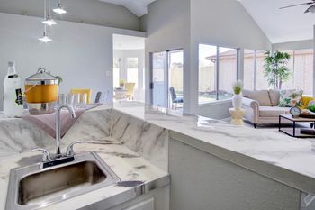 A kitchen with a sink and a living room in the background