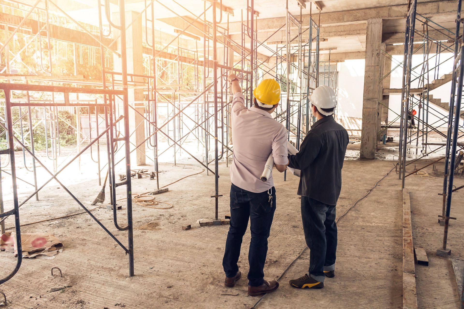 Two construction workers are standing in a building under construction.