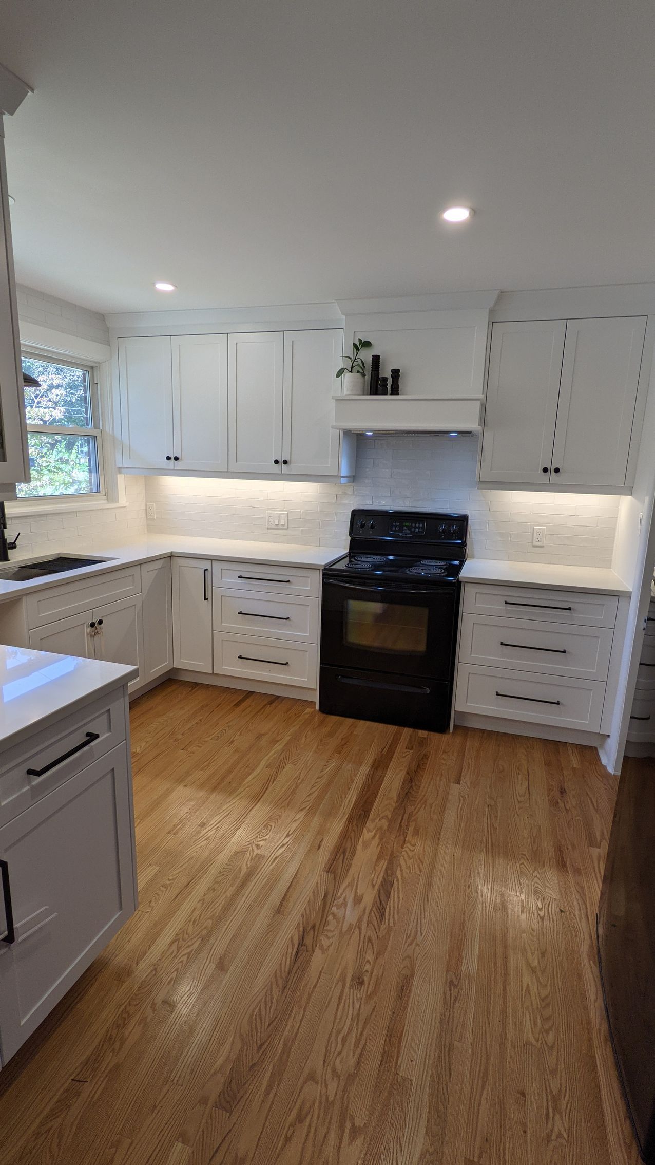 A kitchen with white cabinets , hardwood floors , and a black stove.