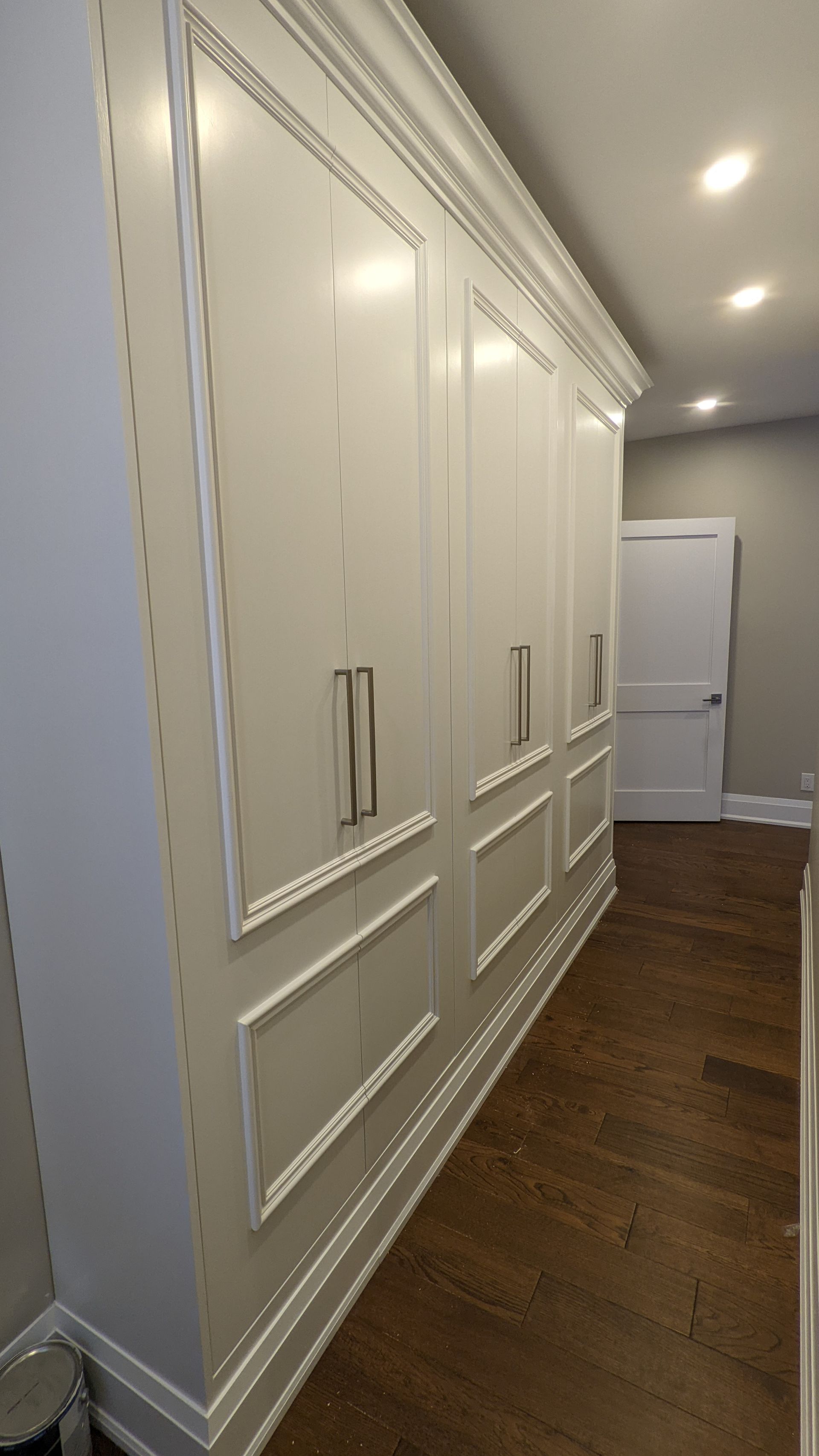 A large white cabinet in a hallway with wooden floors.