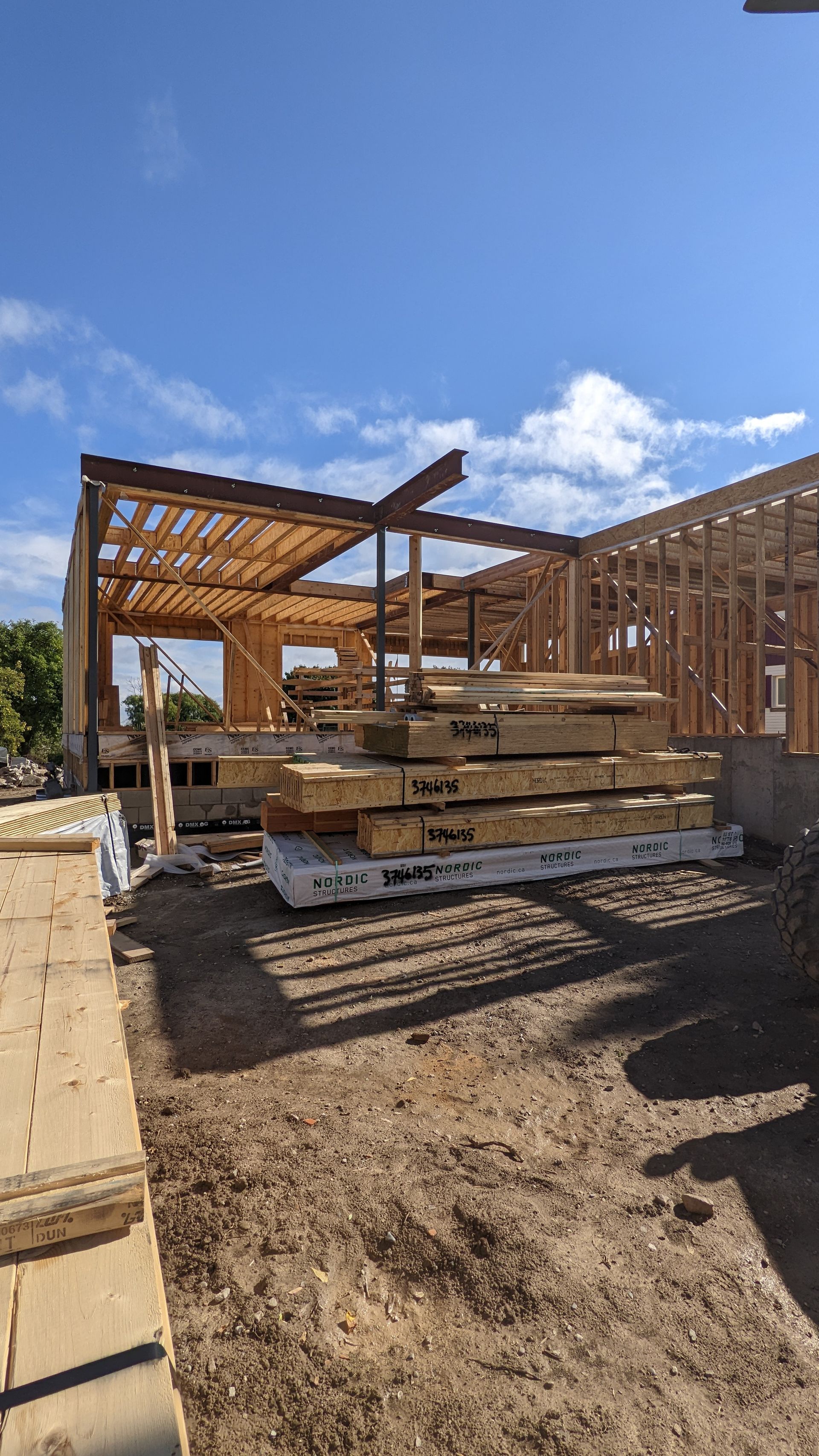 A stack of wood is sitting in the dirt in front of a house under construction.