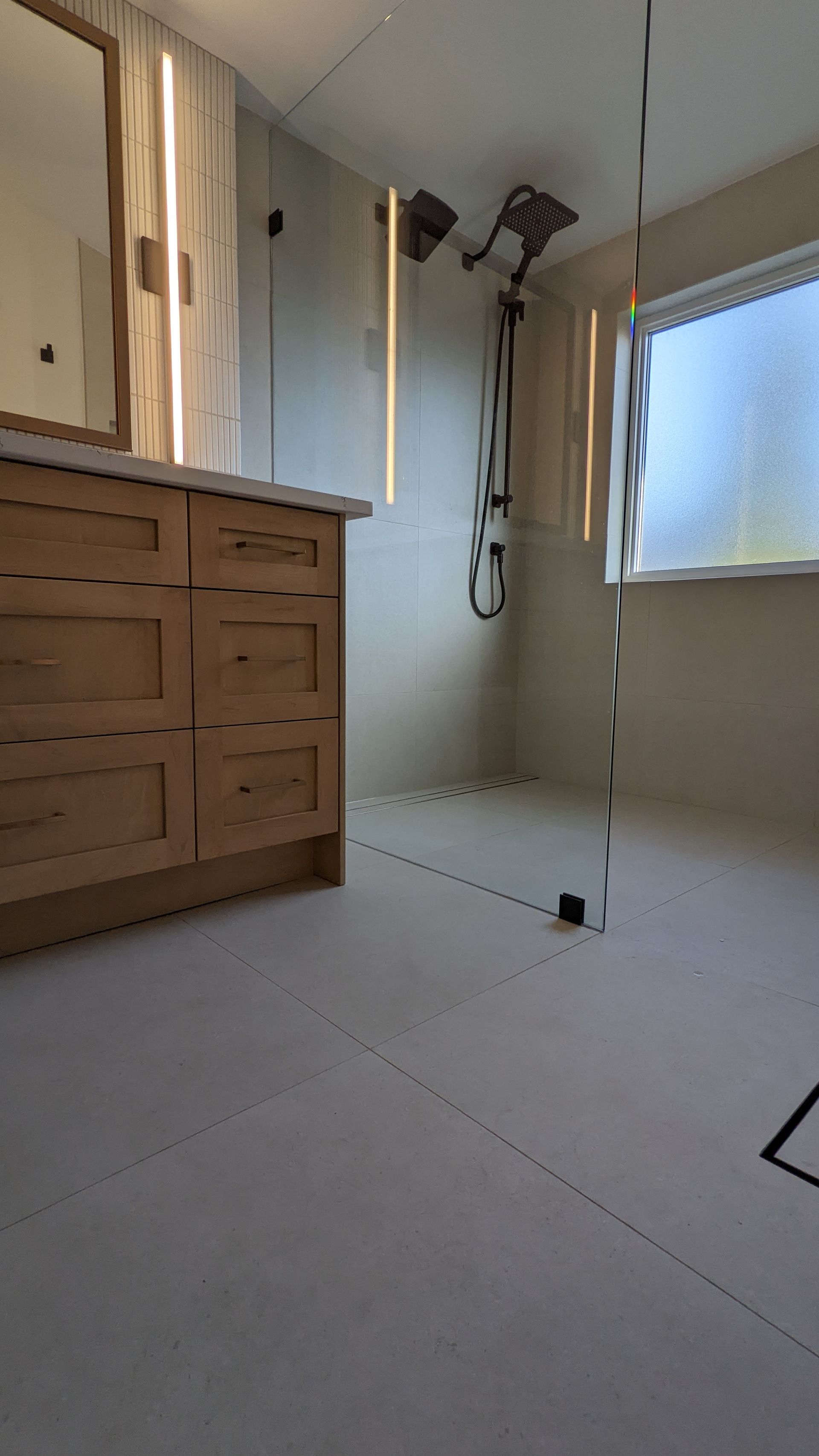 A bathroom with a walk in shower , sink , mirror and window.
