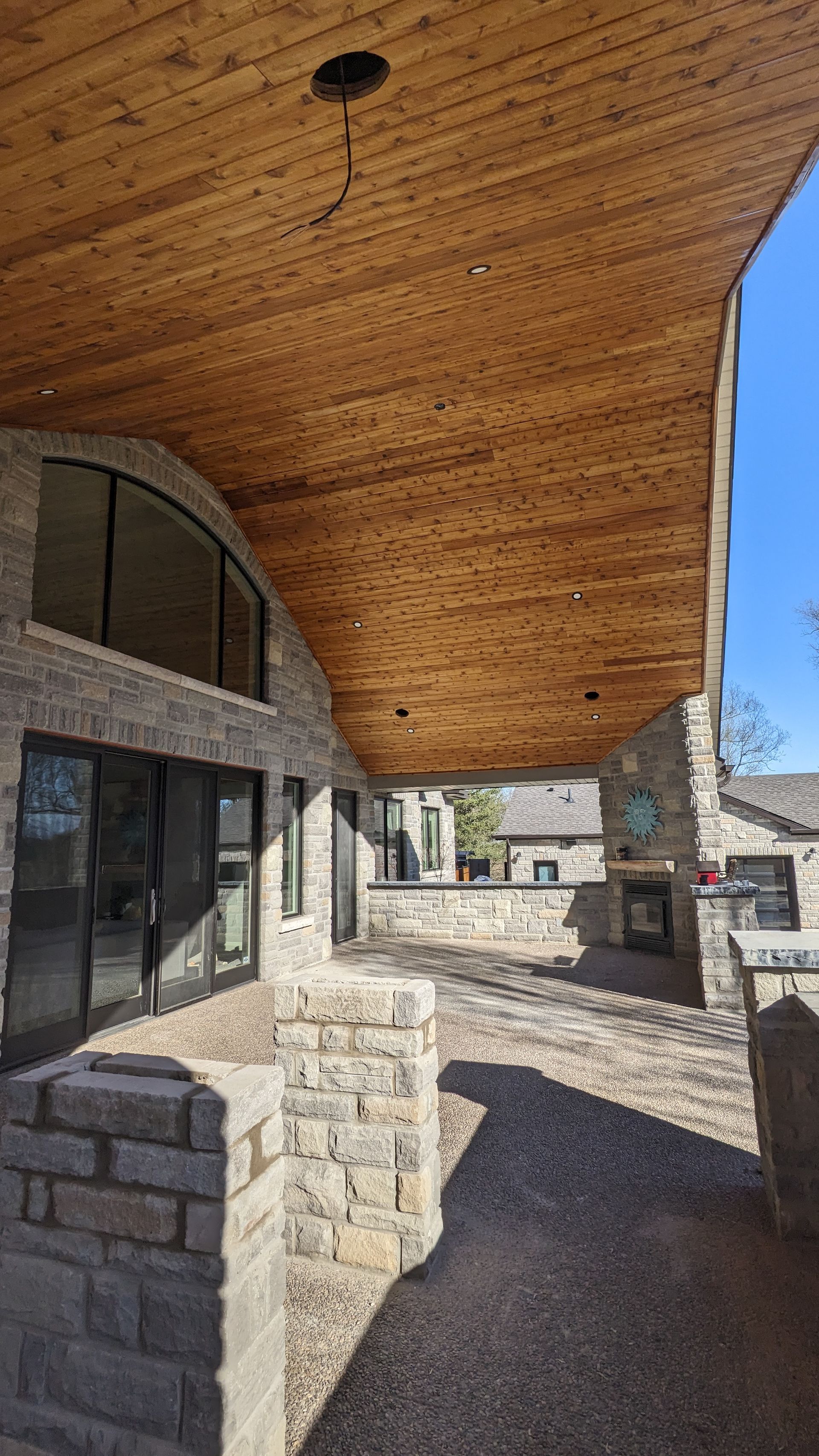 A large covered patio with a wooden ceiling and a stone wall.