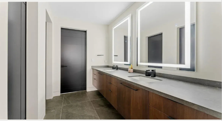A bathroom with a sink , mirror , soap dispenser and flowers.