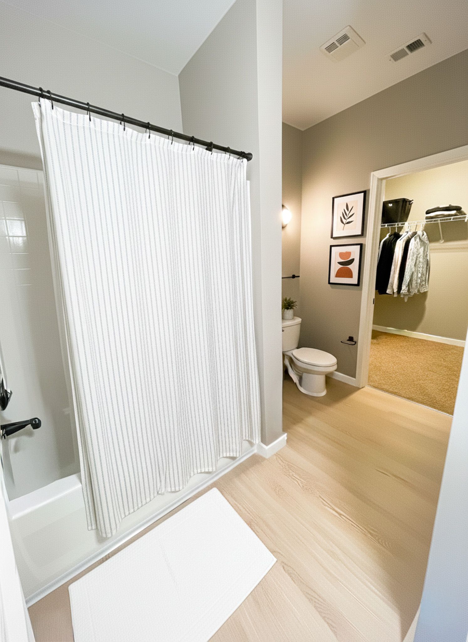 Bathroom with shower/tub, toilet, and doorway to closet; light wood floors, gray walls.