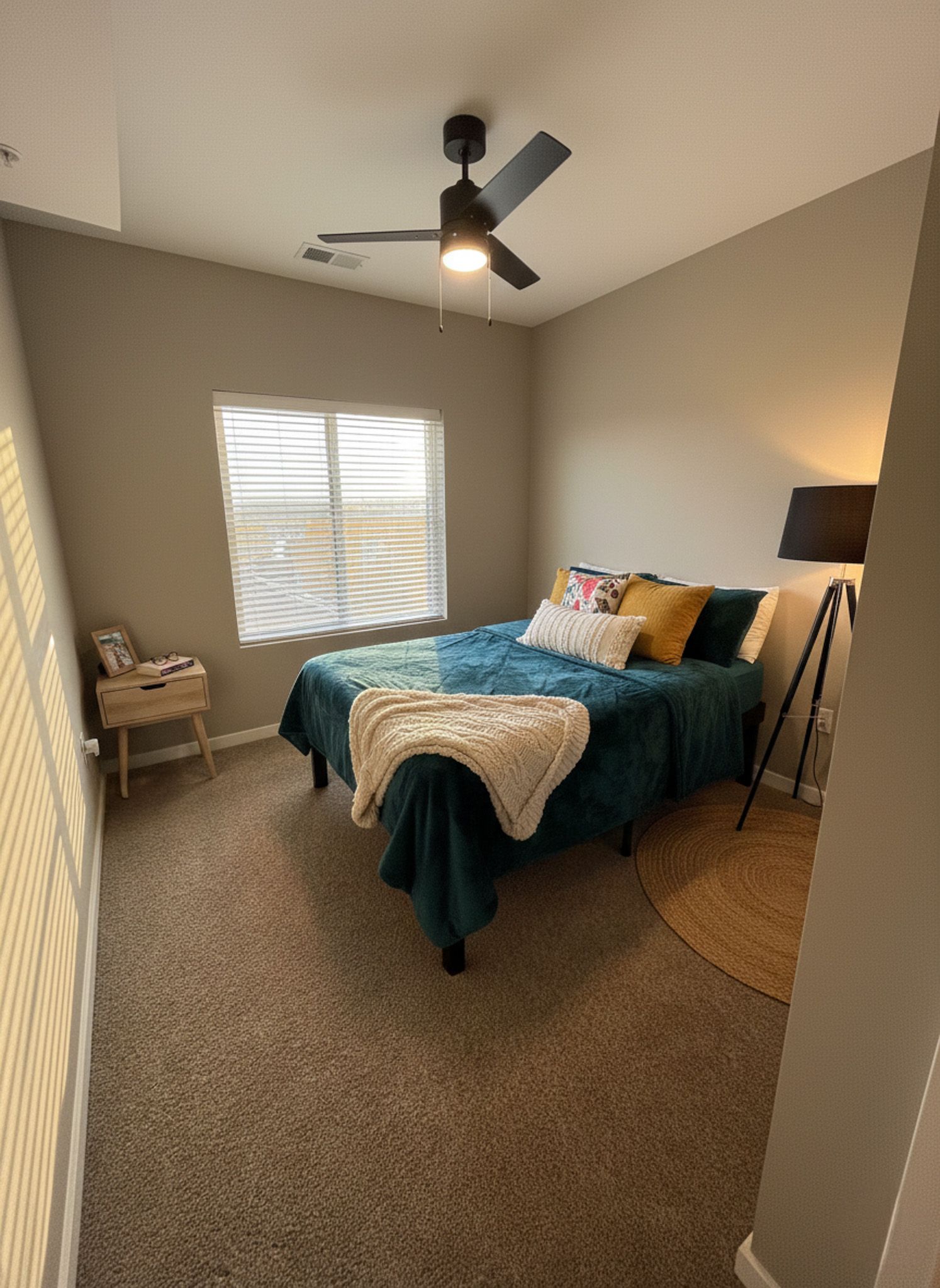 Bedroom with a teal bed, window, side table, and black ceiling fan.