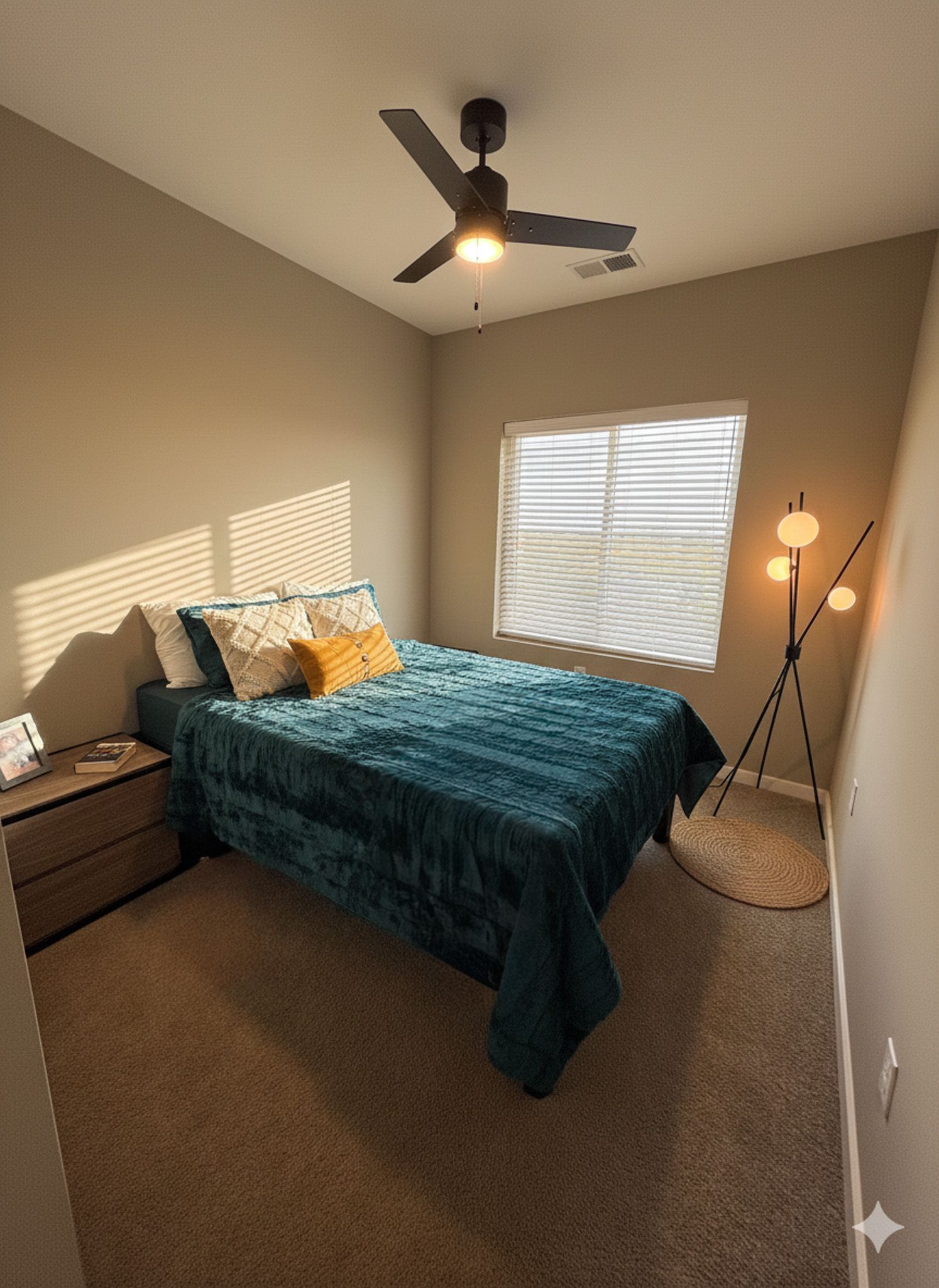 Bedroom with teal bedspread, window with blinds, brown carpet, ceiling fan, and floor lamp.