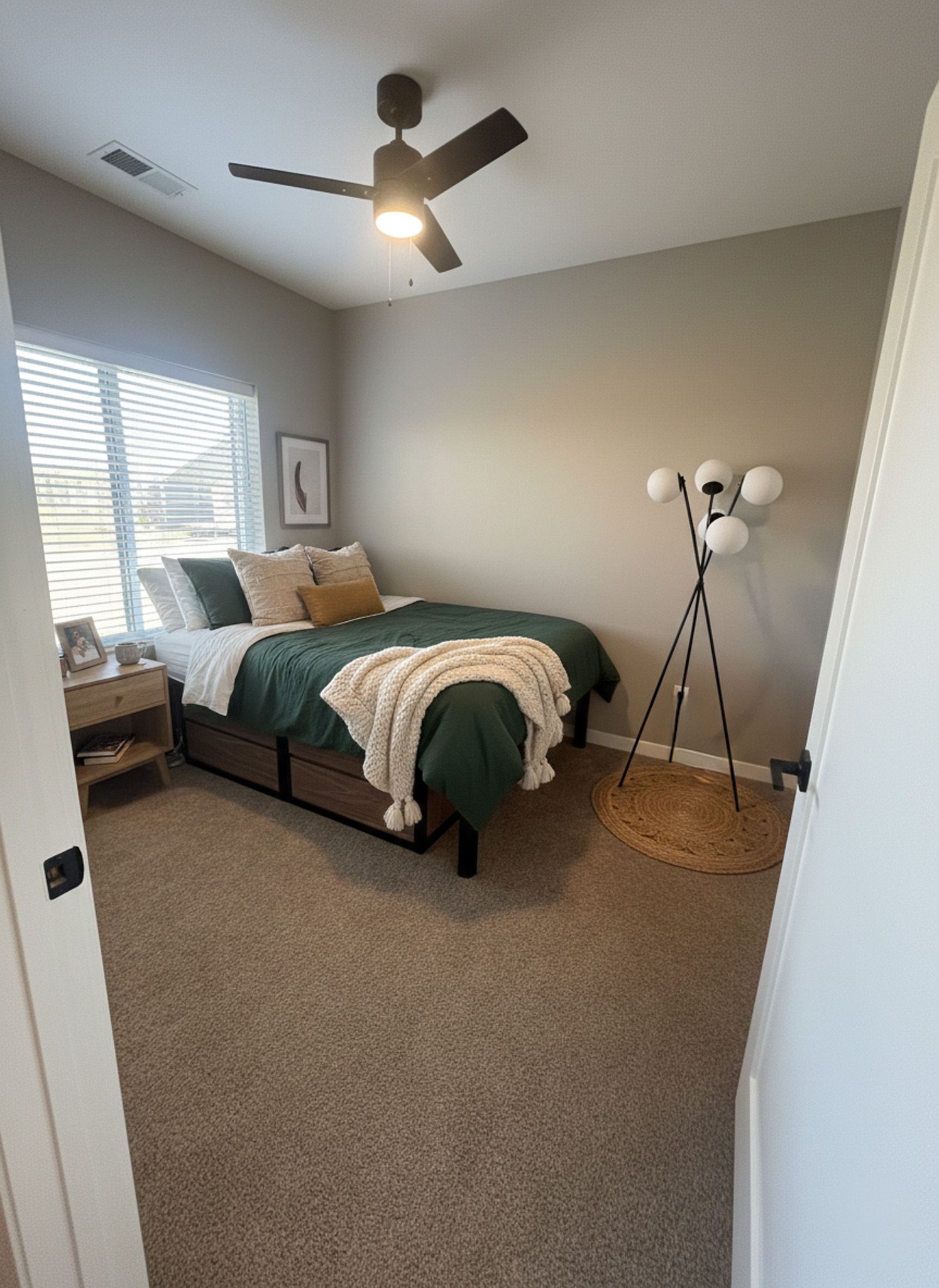Bedroom with a bed, nightstand, lamp, and ceiling fan. Green bedding and a cream-colored throw.
