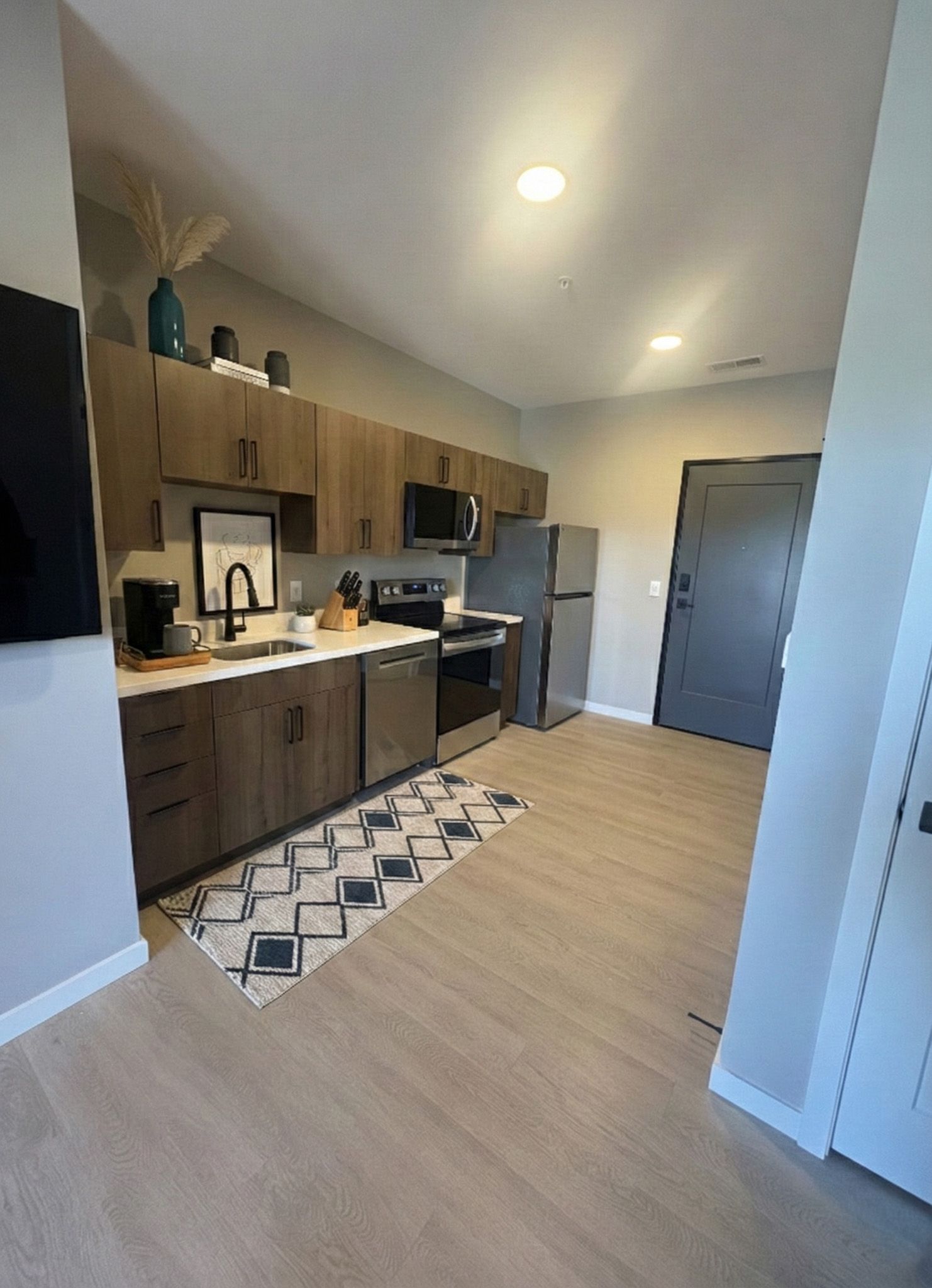 Kitchen with light wood cabinets, stainless steel appliances, and a gray door.