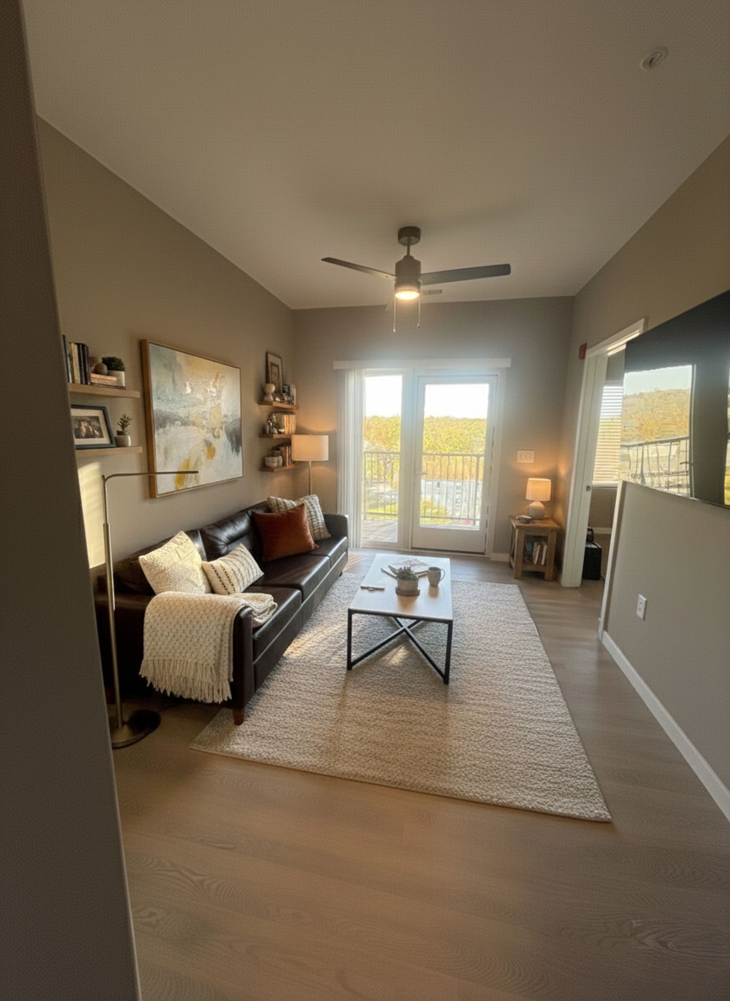 Living room with leather sofa, rug, coffee table, shelves, and balcony access.