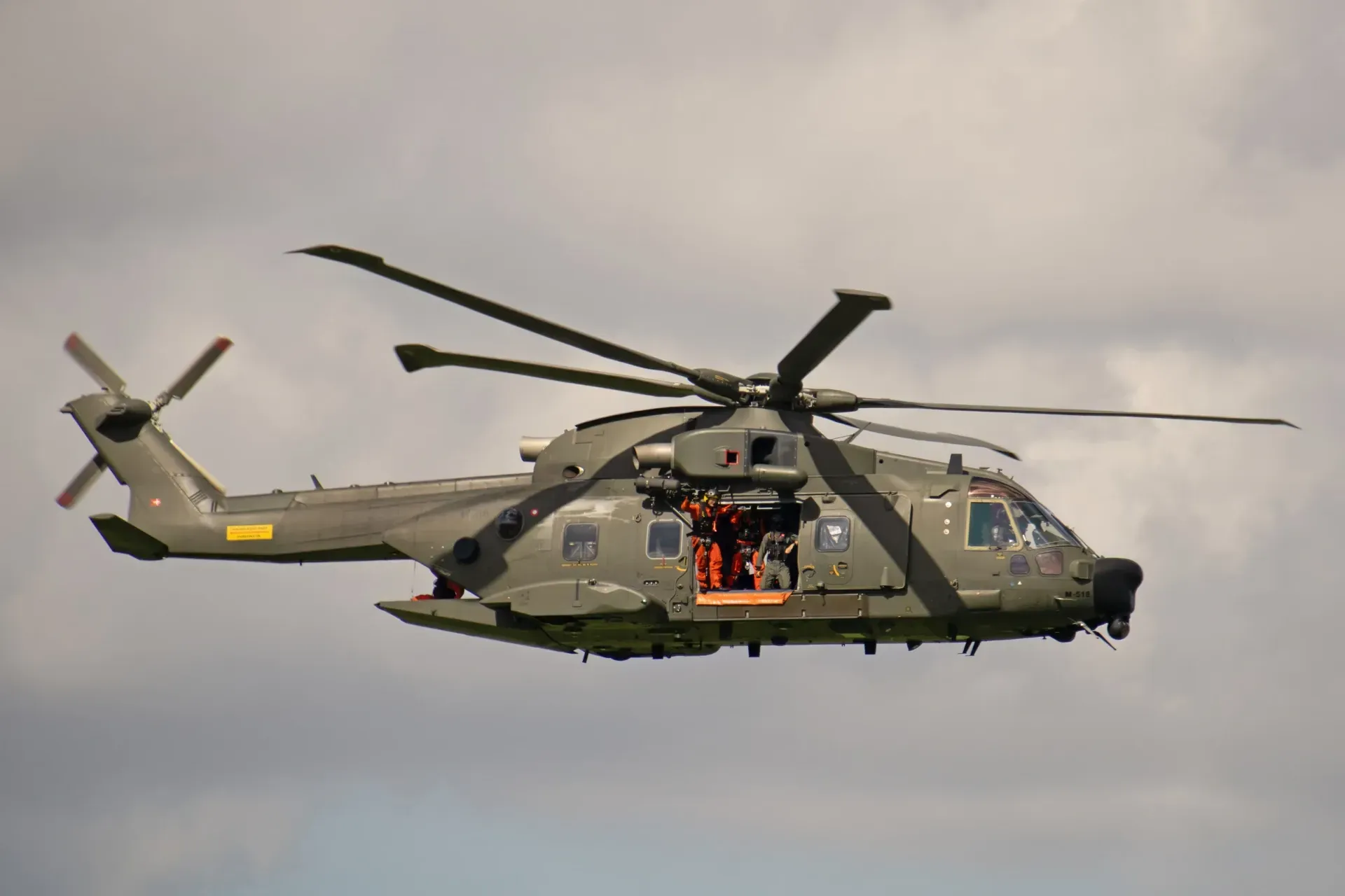  Military helicopter flying with side door open and crew visible.