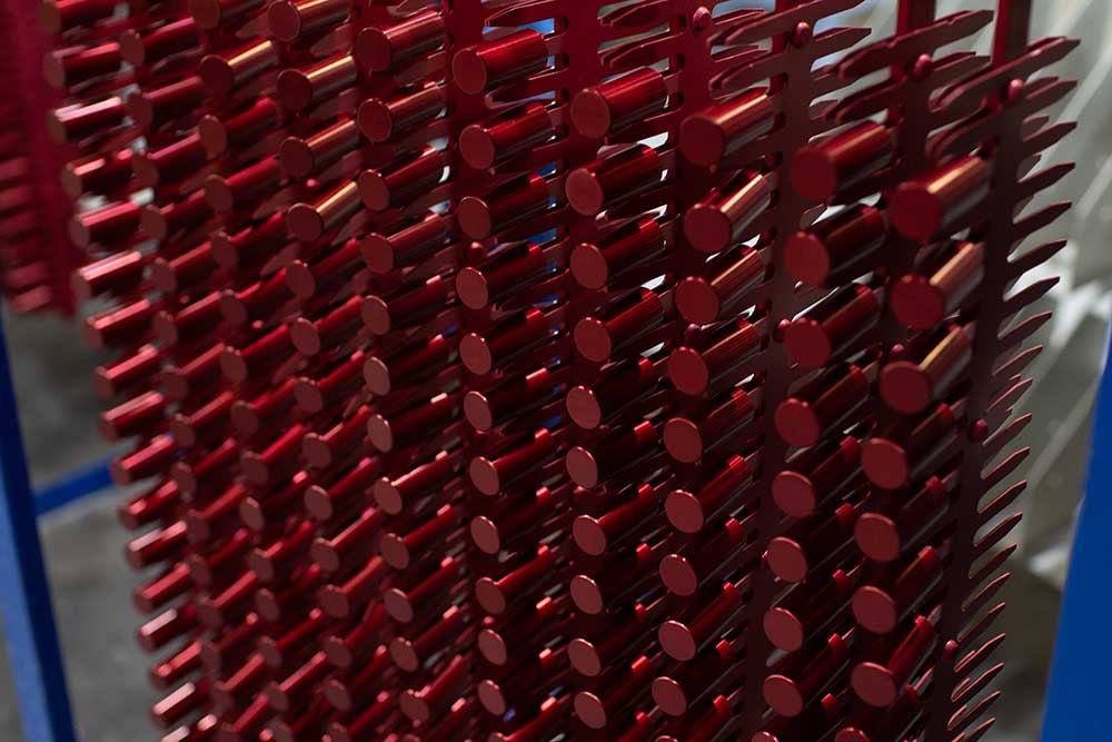 Long silver and red metal pieces hanging on a rack post-sulfuric acid anodizing.
