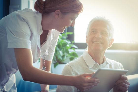 caregiver handing over the tablet to an old man