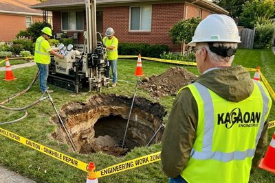 Kagaoan Engineers in high-visibility vests are making a sinkhole repair in a residential lawn using drilling equipment.