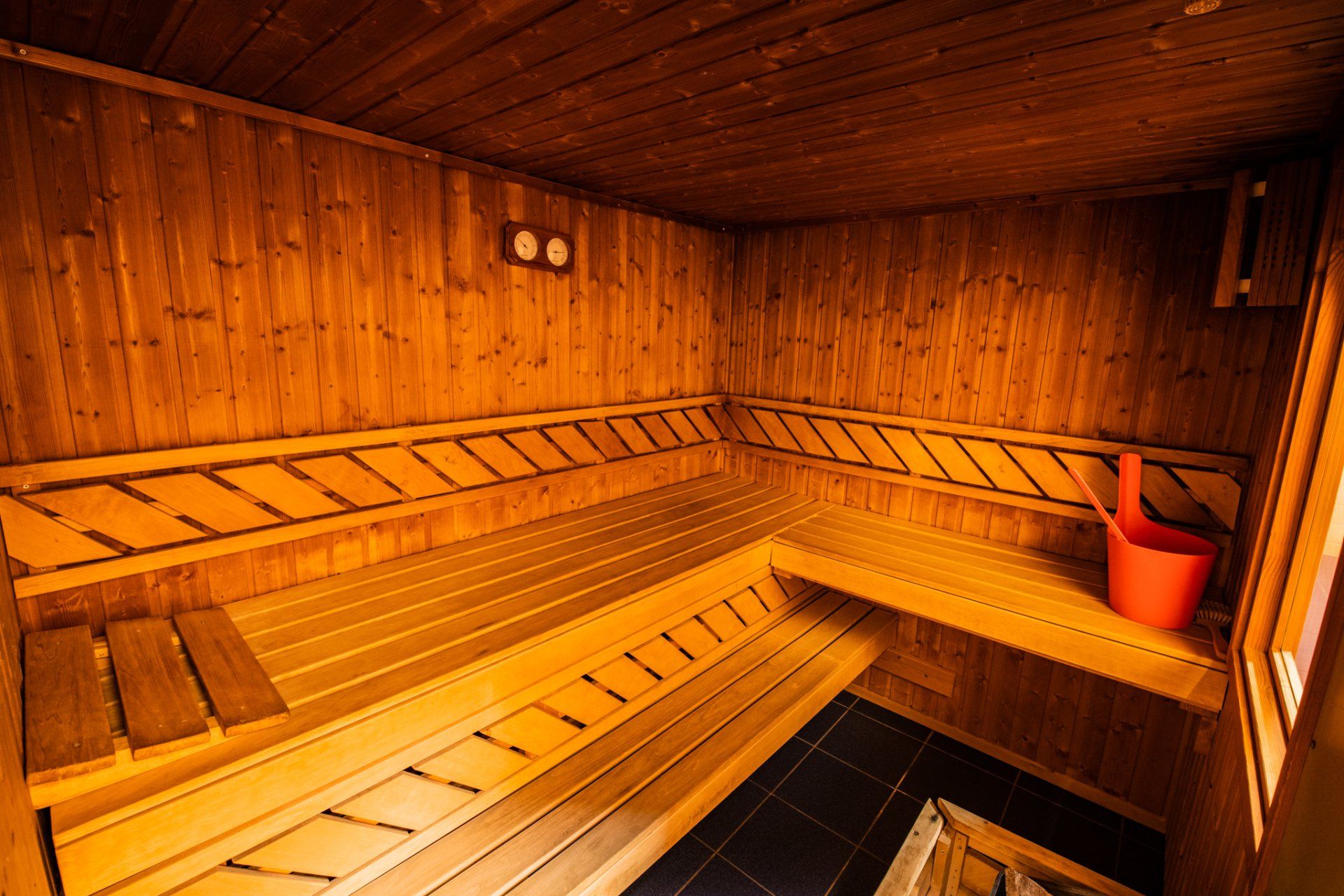 Een houten sauna met een rode emmer op de vloer.