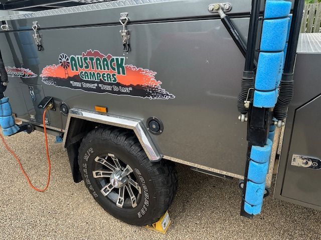 Gray camper trailer with a black tire and blue foam padding. 