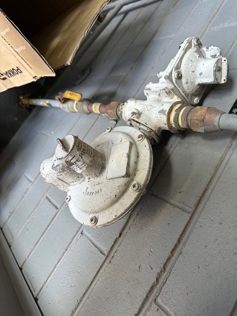 Gas regulator assembly on a brick wall, with pipes and yellow valve — Gas Fitting Services in Bundaberg, QLD