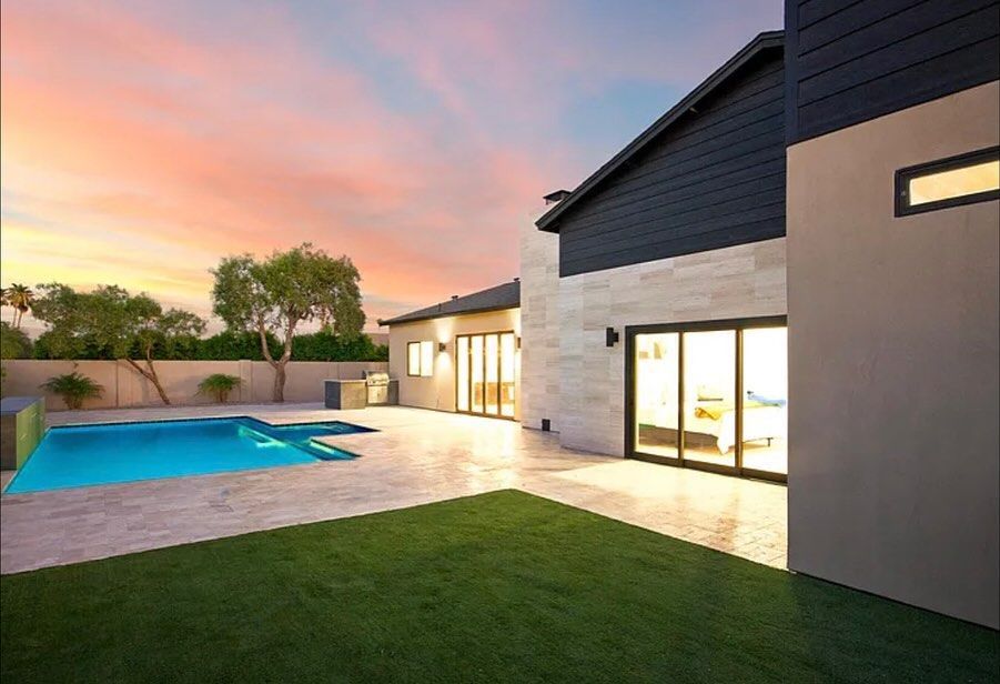 Backyard with a pool, grassy lawn, and modern house at sunset; blue and pink sky.