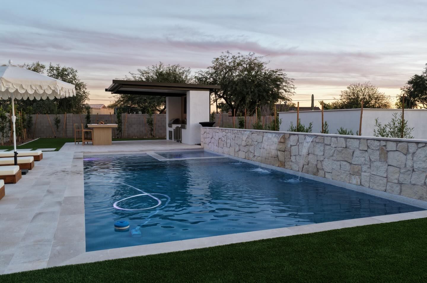 Pool with turquoise water, patio, and stone wall, under a dusky sky.