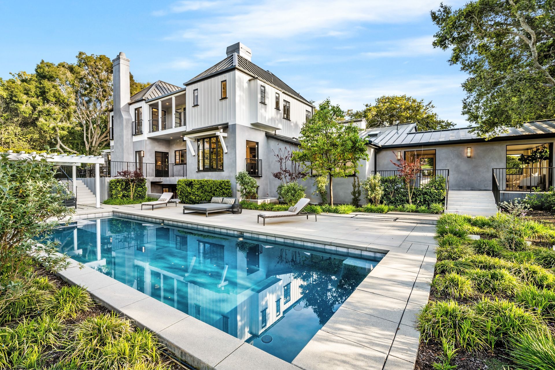 Luxurious white home with pool, lounge chairs, and landscaping under a blue sky.