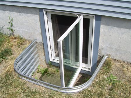Basement window with open door, silver well, grass, gray siding.